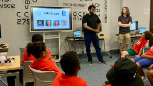 Kids watching presenter, screen says URI AI Lab